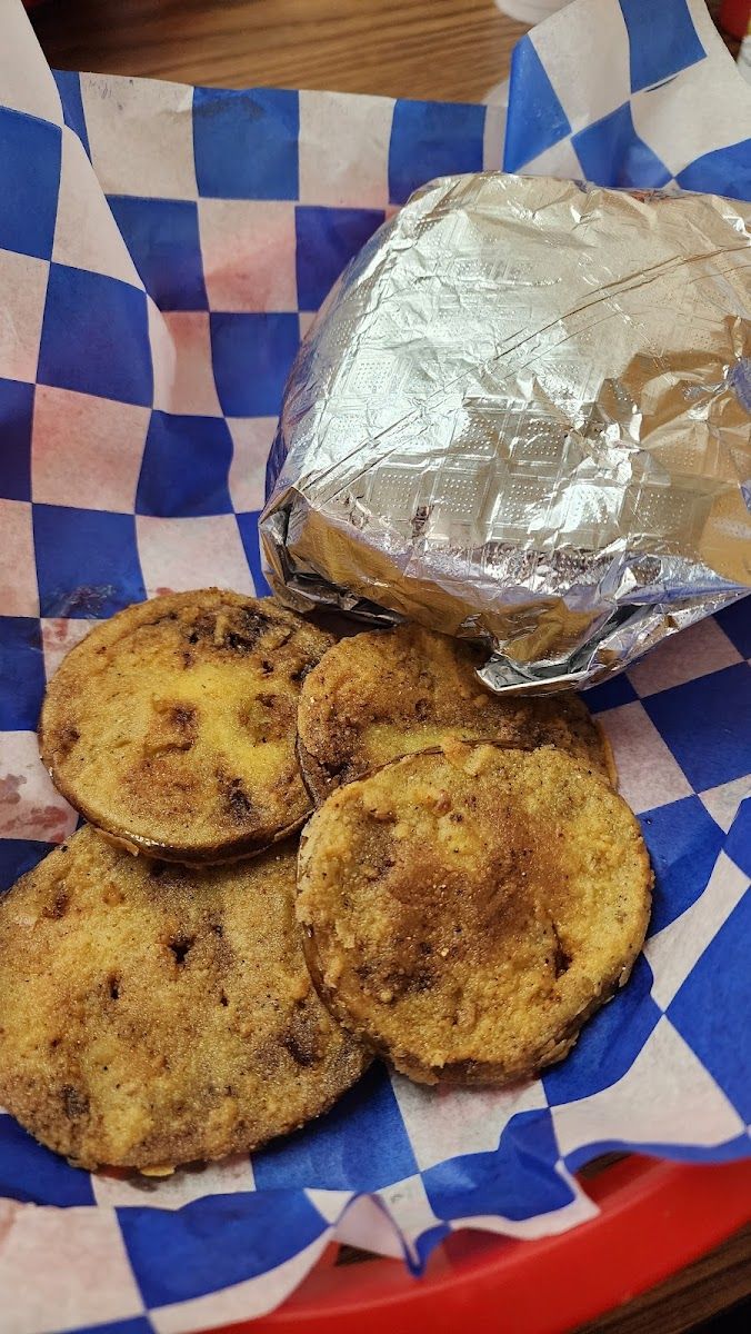Fried green tomato slices in a blue-checked paper basket beside a foil-wrapped sandwich