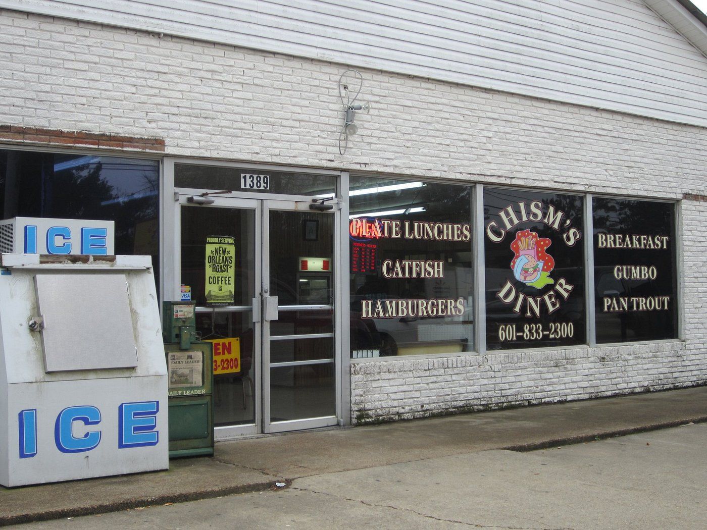 White-brick storefront at 1389 with window lettering: Plate Lunches, Catfish, Hamburgers, Chism's Diner, Breakfast, Gumbo, Pan Trout, 601-833-2300